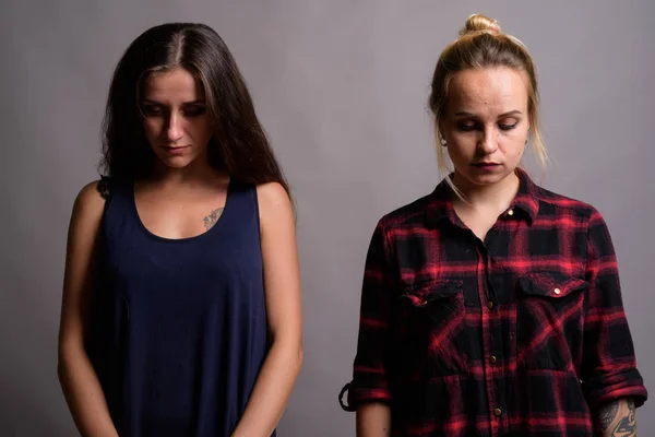 Retrato de dois triste jovem mulher olhando para baixo contra fundo cinza — Fotografia de Stock