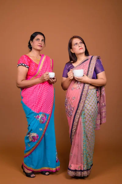Two mature Indian women holding coffee or tea cup