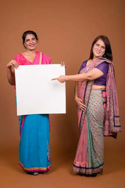 Two mature Indian women holding empty white board with copy space