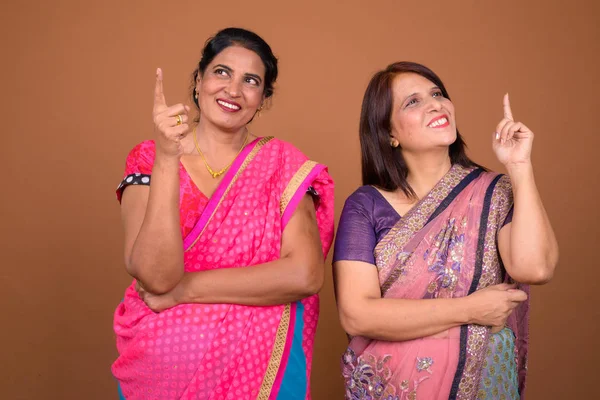 Two happy mature Indian woman thinking and pointing finger up