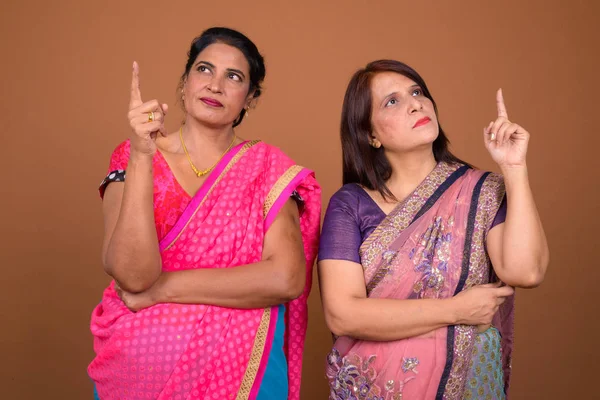 Dos mujeres indias maduras pensando y señalando con el dedo hacia arriba —  Fotos de Stock