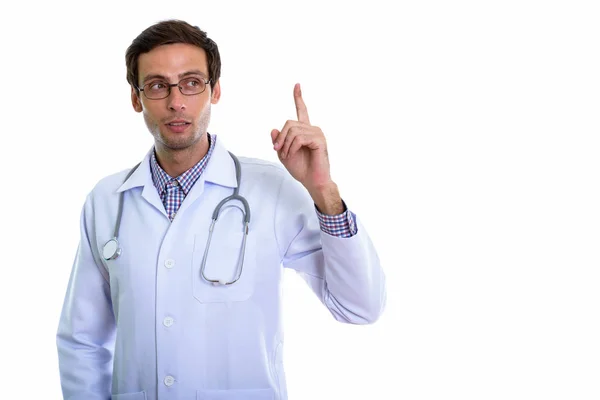 Studio shot of young handsome man doctor thinking while pointing — Stock Photo, Image