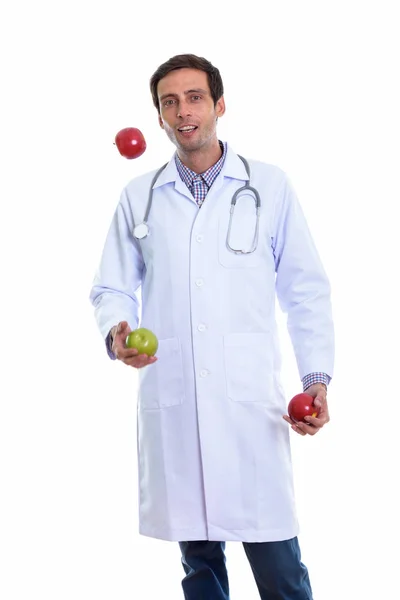 Studio shot of young happy man doctor smiling while juggling gre — Stock Photo, Image