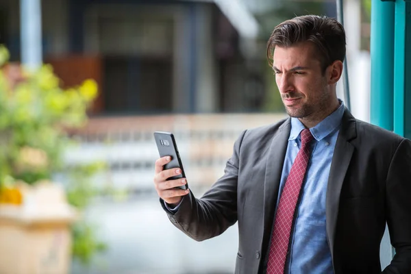 Young handsome Hispanic businessman using phone outdoors — Stock Photo, Image