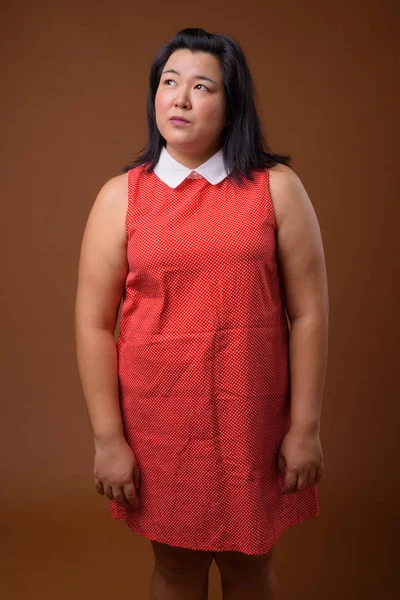 Vackra överviktiga asiatisk kvinna tänkande mot brun bakgrund — Stockfoto