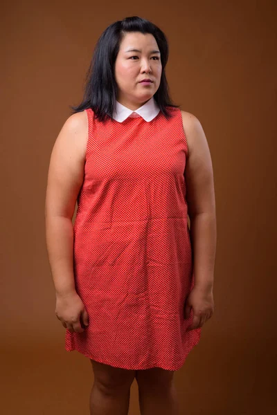 Schöne übergewichtige asiatische Frau vor braunem Hintergrund — Stockfoto