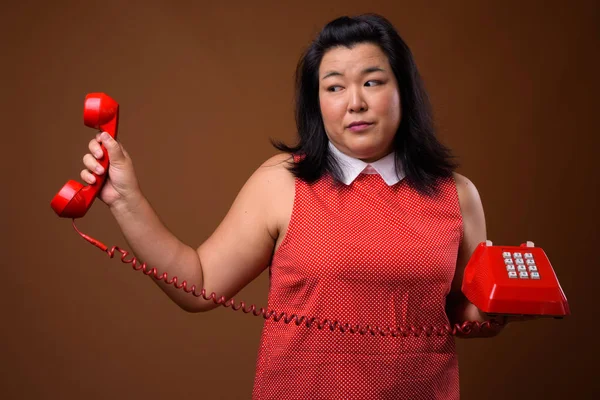 Entediado excesso de peso ásia mulher segurando idade vermelho telefone — Fotografia de Stock