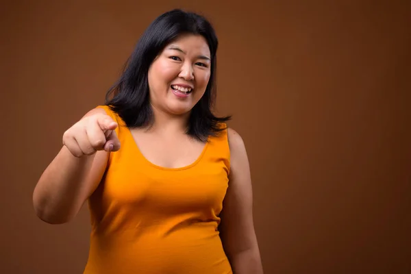 Linda mulher asiática com sobrepeso sorrindo e apontando o dedo para a câmera — Fotografia de Stock