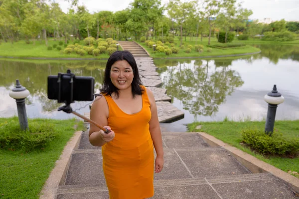 Asijské žena pořizování selfie s mobilním telefonem připojit selfie stick v parku — Stock fotografie