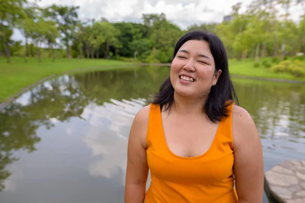 Beautiful overweight Asian woman smiling with eyes closed in park — Stock Photo, Image