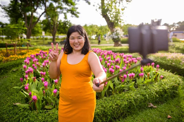 Asian woman taking selfie with mobile phone attach to selfie stick in park — Stock Photo, Image