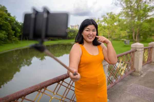 Asian woman taking selfie with mobile phone attach to selfie stick in park — Stock Photo, Image