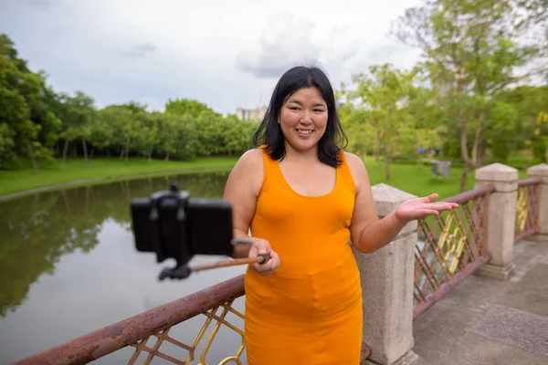 Asian woman taking selfie with mobile phone attach to selfie stick in park — Stock Photo, Image