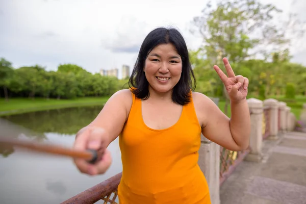 Asian woman taking selfie with mobile phone attach to selfie stick in park — Stock Photo, Image