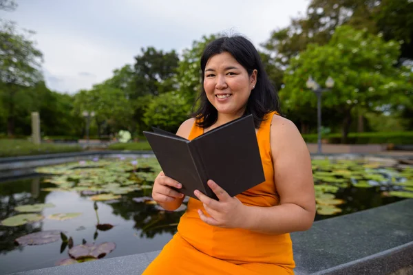 快乐超重亚洲妇女阅读书在公园 — 图库照片