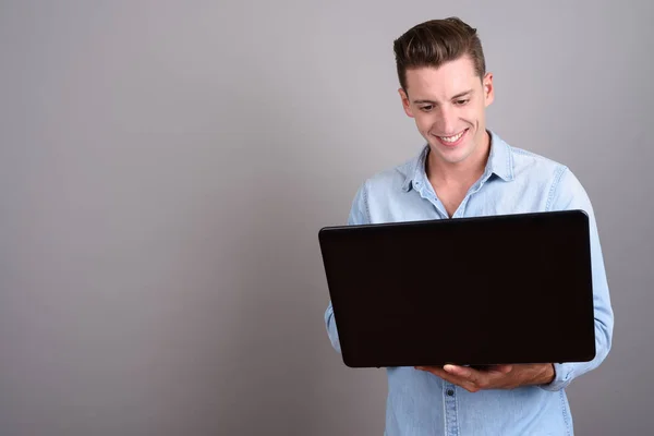 Giovane uomo felice utilizzando computer portatile su sfondo grigio — Foto Stock