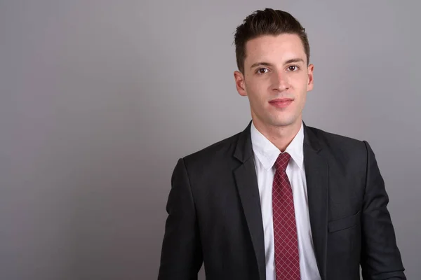 Young handsome businessman wearing suit against gray background — Stock Photo, Image