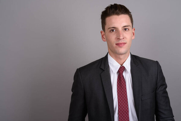 Young handsome businessman wearing suit against gray background