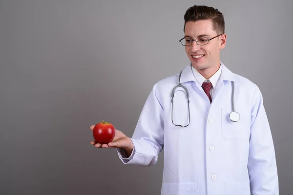 Szczęśliwy młody lekarz trzymając Czerwone jabłko, jednocześnie uśmiechając się — Zdjęcie stockowe
