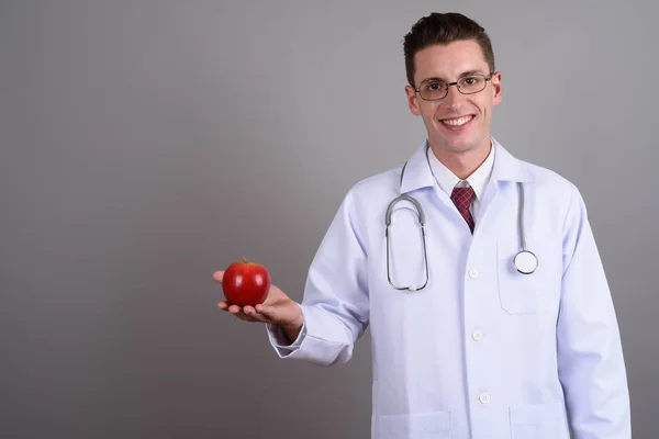 Молодой счастливый человек доктор держит красное яблоко, улыбаясь — стоковое фото