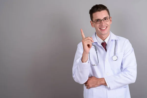 Junger schöner Mann Arzt zeigt mit dem Finger nach oben, während er lächelt — Stockfoto