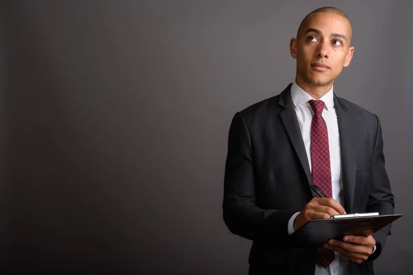 Handsome bald businessman holding clipboard while thinking — Stock Photo, Image