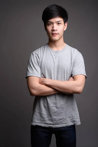 Jonge knappe Aziatische man tegen grijze achtergrond — Stockfoto
