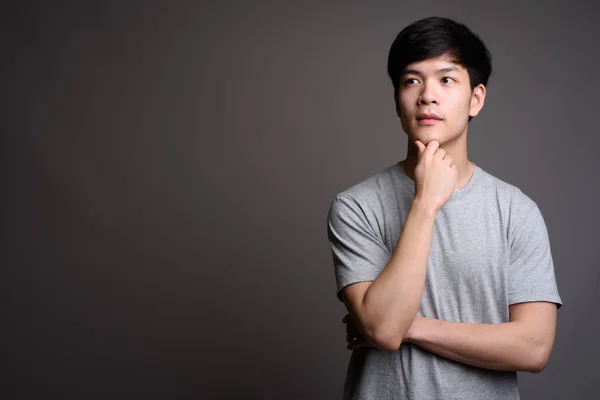 Joven guapo asiático hombre pensando en gris fondo —  Fotos de Stock