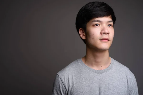 Young handsome Asian man thinking against gray background — Stock Photo, Image