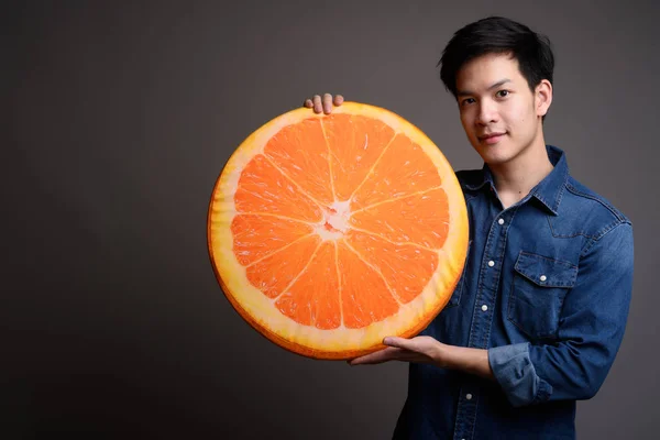 Giovane bello asiatico uomo holding arancio frutta cuscino — Foto Stock