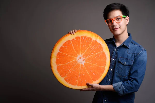 Joven guapo asiático hombre sosteniendo naranja fruta almohada — Foto de Stock