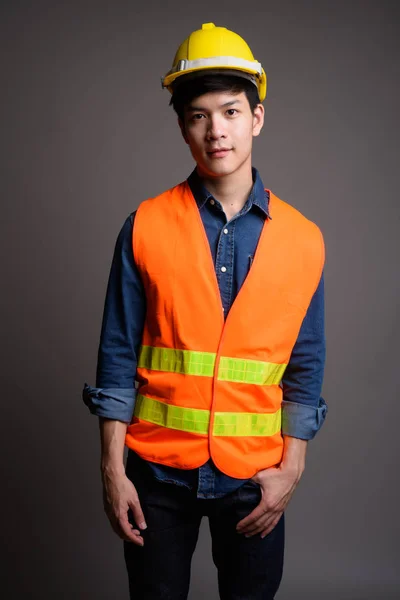 Genç yakışıklı Asya adam inşaat işçisi gri backgr karşı — Stok fotoğraf