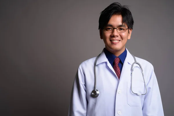 Feliz joven asiático hombre médico sonriendo sobre gris fondo —  Fotos de Stock