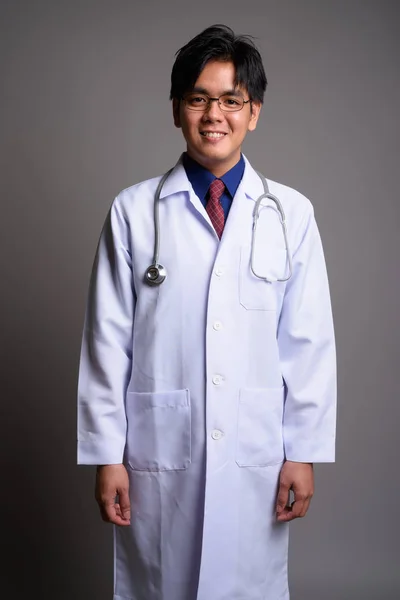 Gelukkig jonge Aziatische man arts glimlachend tegen de grijze achtergrond — Stockfoto