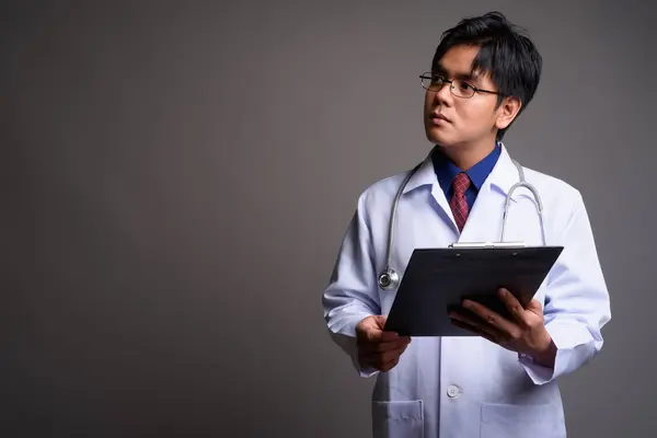 严肃的年轻亚洲人医生拿着剪贴板和思考 — 图库照片