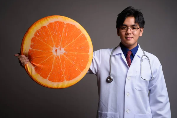 Fiatal ázsiai férfi orvos üzem nagy narancssárga gyümölcs szelet — Stock Fotó