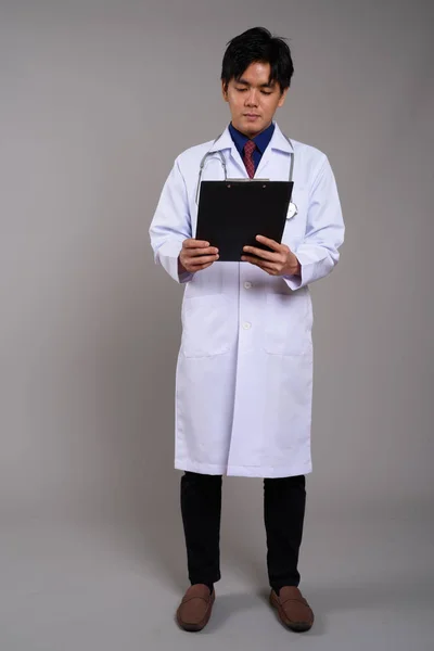 Full length portrait of young Asian man doctor reading clipboard — Stock Photo, Image