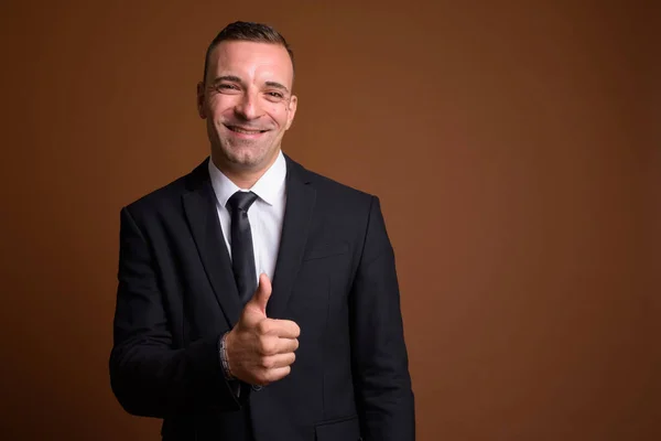Portrait of businessman wearing suit against brown background — Stock Photo, Image