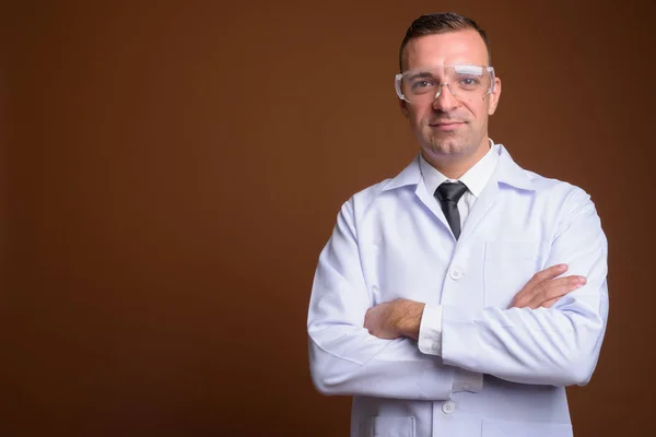 Hombre doctor usando gafas protectoras contra fondo marrón —  Fotos de Stock