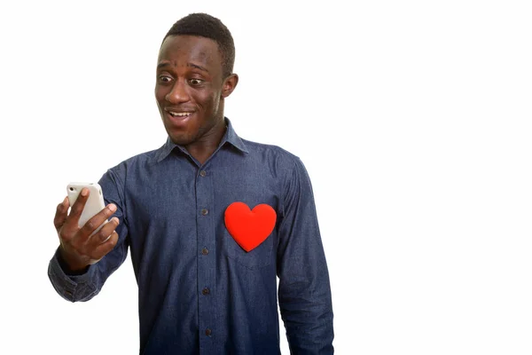 Młody człowiek Afryki szczęśliwy uśmiechający się i przy użyciu telefonu komórkowego z czerwonym — Zdjęcie stockowe