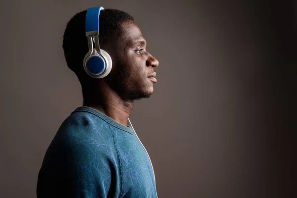 Young African man listening to music against gray background — Stock Photo, Image