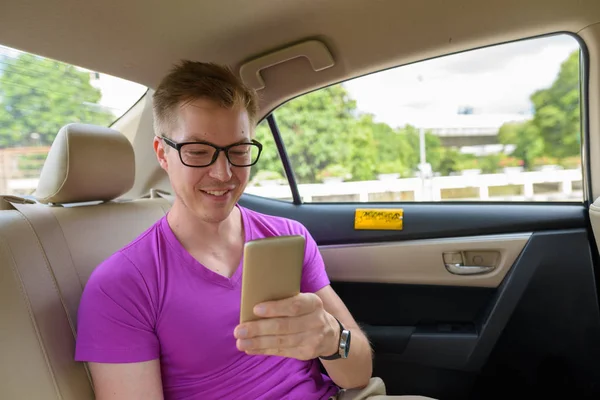 Young happy tourist man inside the car using mobile phone