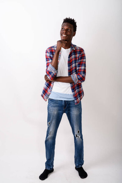 Full body shot of young happy black African man smiling and standing while thinking against white background