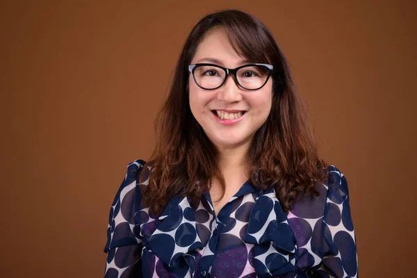 Zralé krásné asijské podnikatelka proti hnědým pozadím — Stock fotografie