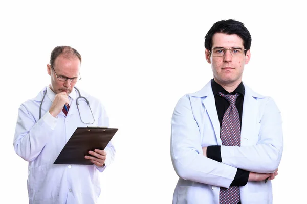 Young man doctor with arms crossed and mature man doctor reading — Stock Photo, Image