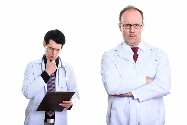 Зрілий чоловік лікар зі схрещеними руками і молодий чоловік лікар читає — стокове фото