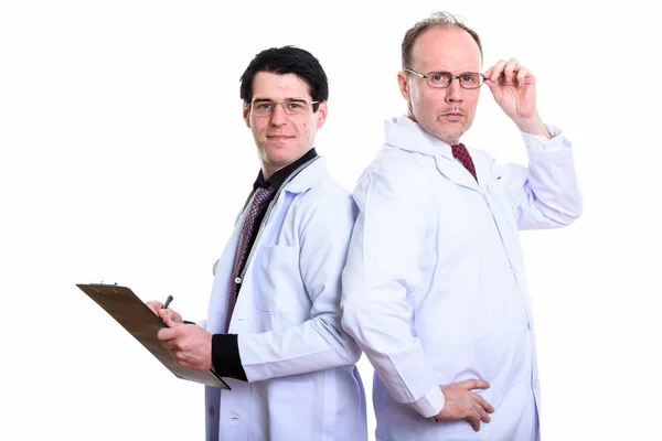 Mature man doctor holding eyeglasses with young man doctor writi — Stock Photo, Image