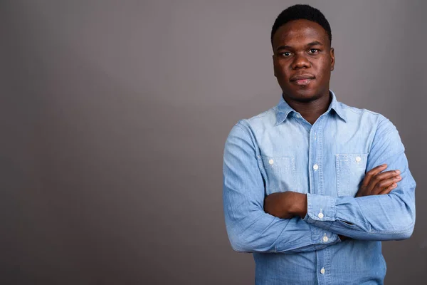 Mladý africký muž v džínové košili na šedém pozadí — Stock fotografie