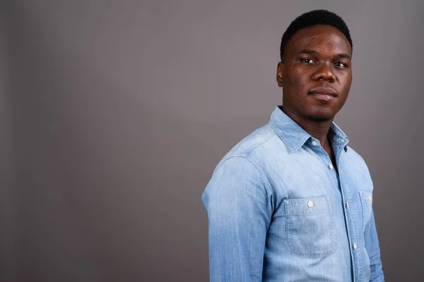 Young African man wearing denim shirt against gray background — Stock Photo, Image