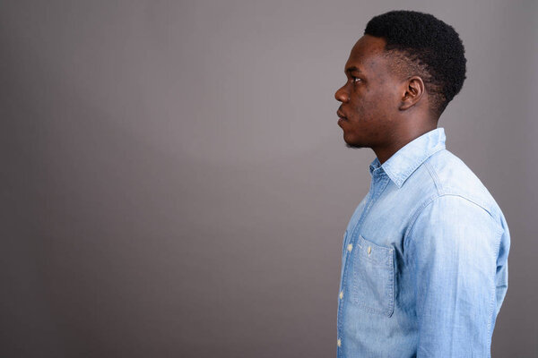 Studio shot of young African man wearing denim shirt against gray background